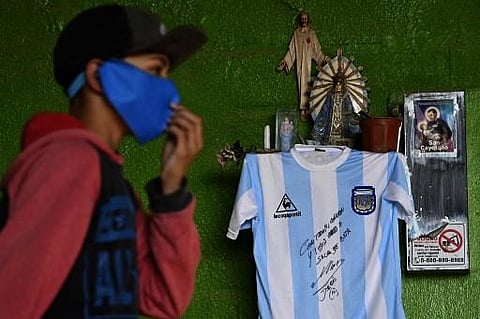 A kid walks past a replica of Argentina's football team jersey used during the final of the FIFA World Cup Mexico '86, handwritten and signed by Argentine former football star Diego Maradona. (Photo | AFP)