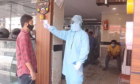 A man giving the sanitizer and thermal check by wearing PPE suit to the customers who came to buy take away food at outside at a restaurant at Ameerpet on fear of corona virus in Hyderabad. (Photo | EPS/sathya keerthi)