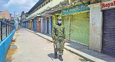 A BBMP marshal patrols the lanes around K R Market, which was sealed down amidst rising Covid-19 cases, in Bengaluru on Tuesday | pandarinath B