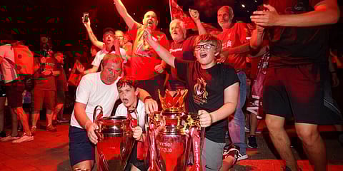 Liverpool supporters with replica Premier League and Champions League trophies as they celebrate outside of Anfield Stadium. (Photo | AP)