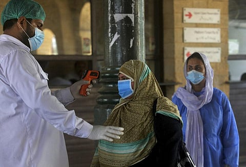 A railway worker checks the body temperature of a woman wearing a protective mask to help curb the spread of the coronavirus, on her arrival at a railway station to board on a train, in Karachi, Pakistan, Saturday, Jan. 6, 2020. (Photo | AP)