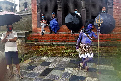 A member of a television crew stands dressed as Hindu god Shiva as Nepalese Hindu devotees wearing masks sit after offering prayers from outside the closed gate of Pashupatinath temple during the holy month of Shrawan in Kathmandu, Nepal, Monday, July 20,