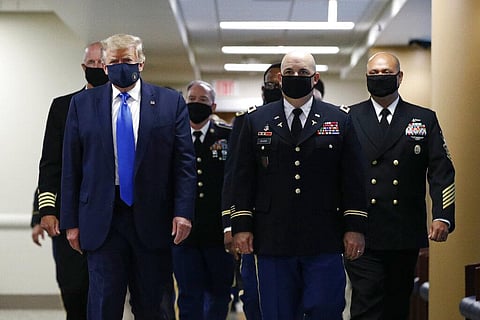 President Donald Trump, foreground left, wears a face mask as he walks with others down a hallway during (Photo | AP)