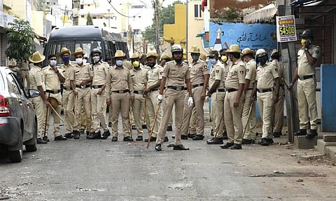 Bengaluru Police stand guard next to charred remains of vehicles vandalised by a mob over a social media post allegedly by a relative of a Congress MLA in Bengaluru. (Photo | Vinod Kumar T, EPS)