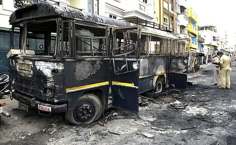 Police stand guard next to charred remains of vehicles vandalised by a mob over a social media post allegedly by a relative of a Congress MLA in Bengaluru. (Photo | Vinod Kumar T/EPS)
