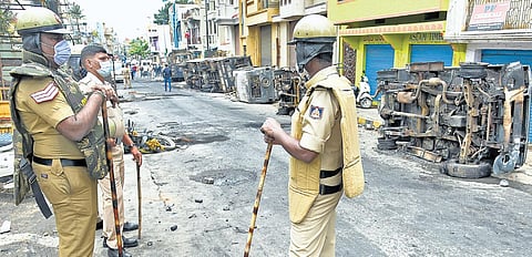 Policemen stand guard next to the charred Curfew clamped, security up in KB Sandra remains of vandalised vehicles. (Photo | Vinod Kumar T, EPS)