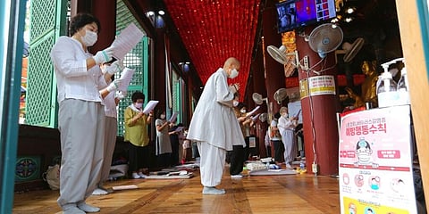 People wearing face masks pray while maintaining social distancing during a service at the Chogyesa temple in Seoul. (Photo | AP)