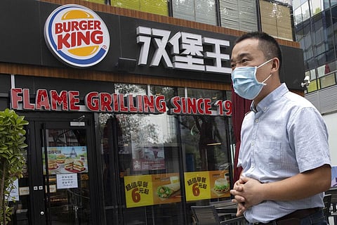 A man wearing a mask to curb the spread of the coronavirus walks past a Burger King restaurant franchise in Beijing. (Photo | AP)