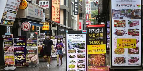 People wearing face masks to help protect against the spread of the coronavirus pass by restaurant banners in Seoul. (Photo | AP)