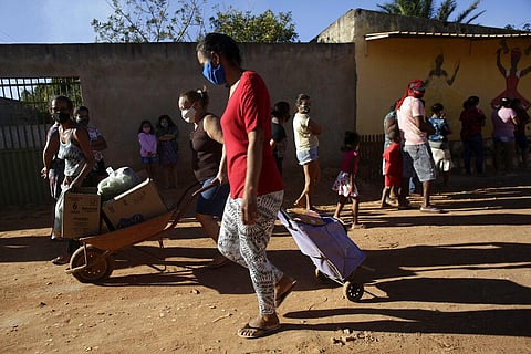 Wearing a masks to curb the spread of coronavirus, women cart away in a wheelbarrow a handout of produce and basic supplies, in the Sol Nascente community, on the outskirts of Brasilia (Photo | AP)