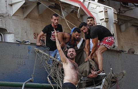 Civilians help to evacuate an injured sailor from a ship which was docked near the explosion scene that hit the seaport of Beirut, Lebanon, Tuesday. (Photo | AP)