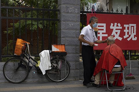 A street barber wearing a face mask to protect against the coronavirus attends to his customer near a banner on the pandemi in Beijing, Thursday, July 30, 2020. (Photo | AP)