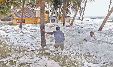 Two persons wading through the water  thrown to the shore by strong waves at Chellanam on Thursday