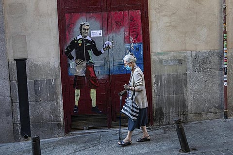 An elderly woman wearing a face mask to protect against the coronavirus walks past a painting named 'to be or not to be' by artist TVBOY.  (Photo | AP)