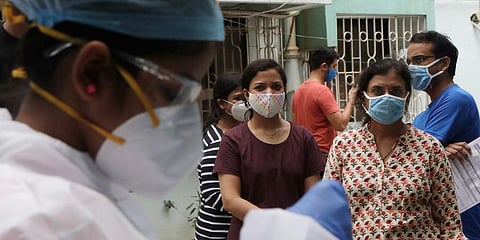 People watch as health workers take swab sample to test for COVID-19 outside a residential building in Mumbai. (Photo | AP)