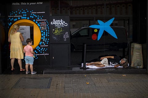 A child looks at a man sleeping outside a CaixaBank brach office in Barcelona, Spain. (File photo | AP)