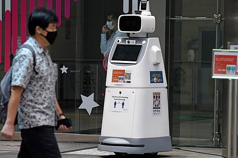 A man wearing a face mask walks past a safe distancing ambassador robot outside an office building in Singapore. (Photo | AFP)