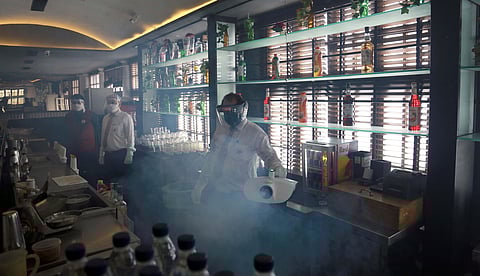 An employee wearing a face shield sanitizes an alcohol cabinet inside QBA Bar ahead of resumption of services in New Delhi.(Photo | EPS/Shekhar Yadav)