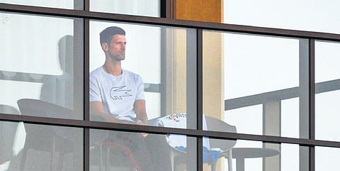 Novak Djokovic on his hotel balcony in Adelaide on Monday. (right) Players being escorted to training sessions in Melbourne | afp/AP