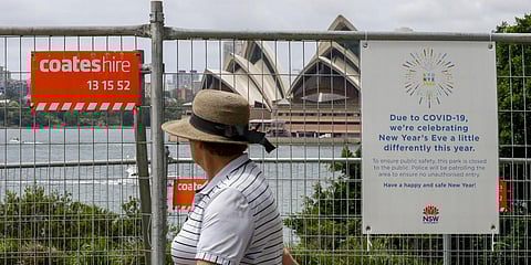 A woman walks past a fence with a COVID-19 warning near the harbour foreshore in Sydney. (File photo| AP)