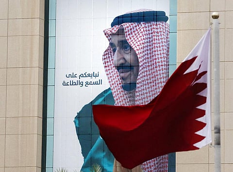 In this Dec. 9, 2019, file photo, a Qatari flag flies in front of a banner showing Saudi King Salman with Arabic writing. (Photo | AP)