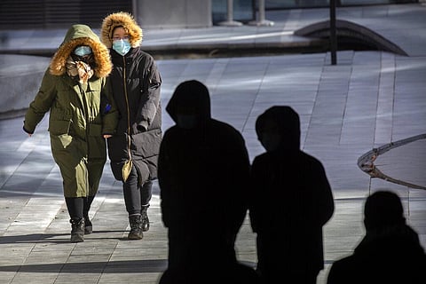 People wearing face masks to protect against the coronavirus walk on an unseasonably cold day at an office and shopping complex in Beijing. (Photo | AP)