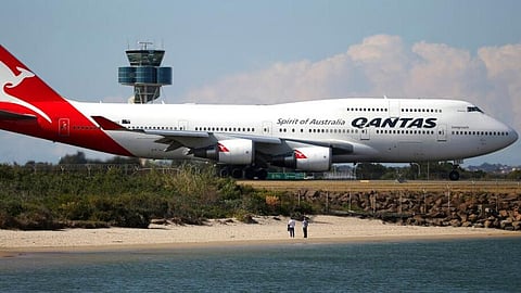 People watch from a beach as a Qantas plane taxies on the runway at Sydney Airport.