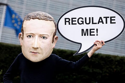 An activist wearing a mask depicting Facebook CEO Mark Zuckerberg holds a banner reading 'Regulate me' outside European Commission building in Brussels. (File photo | AFP)