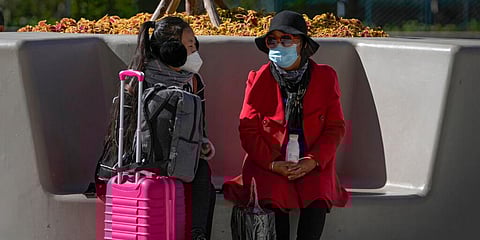 Women wearing face masks chat each other on a bench outside a shopping mall in Beijing. (Photo | AP)