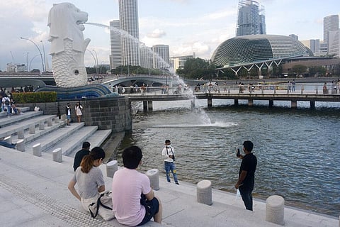 A man wearing a face mask poses for a photo with the Merlion statue in the background. (Photo | AP)