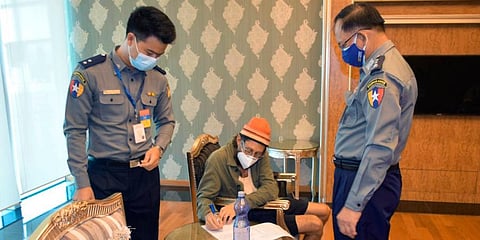 American journalist Danny Fester writes on a document while seated between two police officers at the Naypyitaw International Airport in Naypyitaw, Myanmar. (Photo | AP)