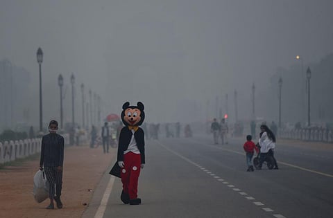 A man is seen walking wearing a mickey mouse costume at Rajpath, which is covered by thick layer of smog. (Photo | PTI)