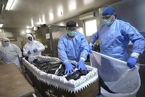 Members of the medical staff place the body of a COVID-19 victim in a coffin together with funeral house employees at the University Emergency Hospital morgue in Bucharest, Romania. (Photo | AP)