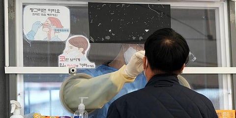 A medical worker in a booth takes a nasal sample from a man at a makeshift testing site in Seoul, South Korea. (Photo | AP)