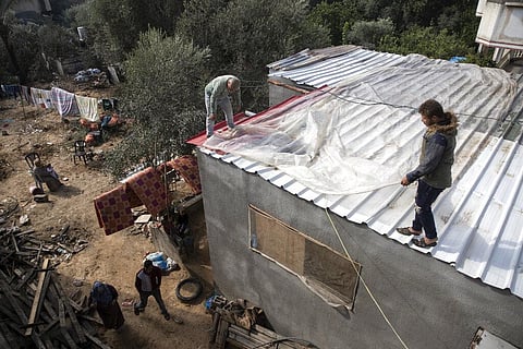 Palestinians cover the roof of their house with nylon to protect it from rain leaks after it was damaged during the 11-day Gaza war (Photo | AP)