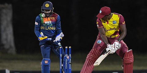 Rovman Powell (R) of West Indies is bowled as the ball is stuck in Sri Lankan Niroshan Dickwella's (L) helmet during a T20I match in Osbourn. (File photo| AFP)