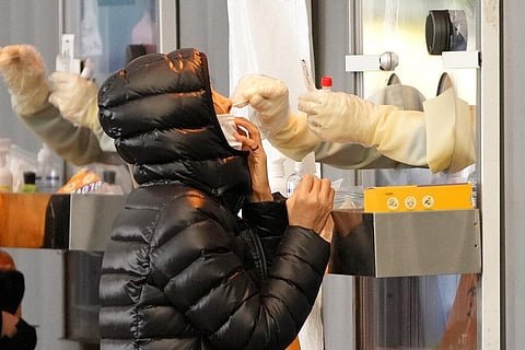 A medical worker wearing protective gear in a booth, takes sample from a woman at a temporary screening clinic for the coronavirus in Seoul (Photo | AP)