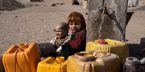 Two Afghan children sit next to a spigot as people of Kamar Kalagh village outside Herat, Afghanistan, try to fill their plastic containers with water. (Photo | AP)