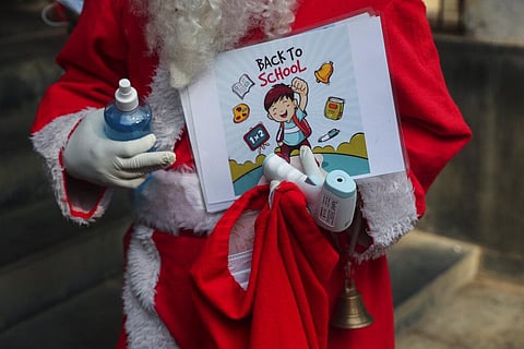 A man dress as Santa Claus holds a bottle of sanitizer and a thermometer as students arrive to attend classes at a school in Mumbai. (Photo | AP)