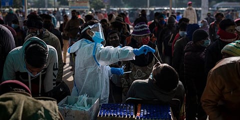 A health worker collects a swab sample of a passenger to test for COVID-19 as others wait for their turn at a train station in New Delhi. (Photo | AP)