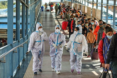 Health workers walk past the passengers waiting in a queue during Covid-19 testing at Katra railway station, amid the threat of spreading of the new Covid-19 variant 'Omicron', in Jammu. (Photo | PTI)