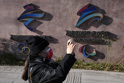A woman wearing takes photos near the logos for the Beijing Winter Olympics and Paralympics in Beijing, China, Tuesday, Nov. 9, 2021. (Photo | AP)