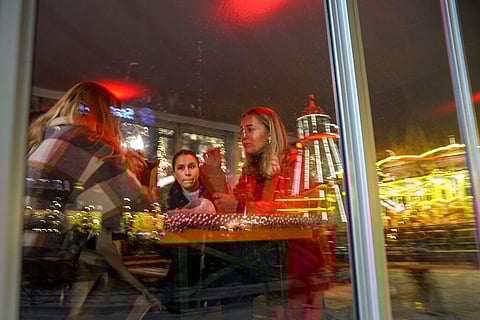 People sit in a street side cafe as an alley hanging with decorations ahead of Christmas reflected in a window in Oslo, Norway. (Photo | AP)