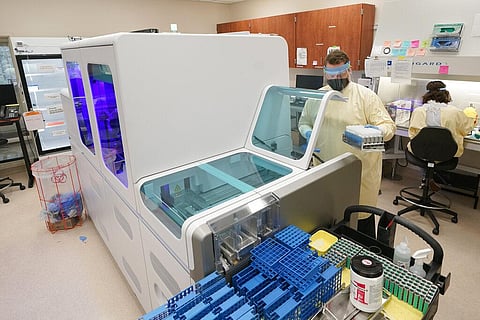 Steven Grimmett, a microbiologist on the COVID-19 team at the Washington State Dept. of Health's Public Health Laboratory, holds samples near a machine. (Photo | AP)