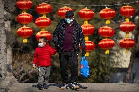 A man and child wearing face masks to protect against the spread of the coronavirus walk past lanterns at a public park in Beijing (Photo | AP)