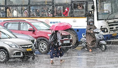 A woman crosses the road through the pouring rain, in Bengaluru on Friday. Many parts of the city received unseasonal showers | AshishKrishna H P