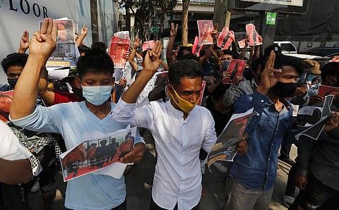 Myanmar nationals living in Thailand hold pictures of Myanmar leader Aung San Suu Kyi gesture with a three-fingers salute, a symbol of resistance. (Photo | AP)