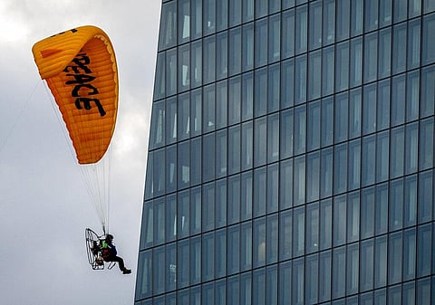 An activist of environmental organization Greenpeace flies with a motorized paraglider past the European Central Bank in Frankfurt (Photo | AP)
