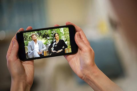 A man watches a phone screen showing an interview of Prince Harry and Meghan, The Duchess of Sussex, by Oprah Winfrey. (Photo | AP)