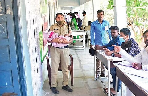 Constable Kavitha from the Bibinagar police station looks after a baby while her mother casts her vote in the Graduate MLC elections, at a polling station in ZPHS Bibinagar on Sunday